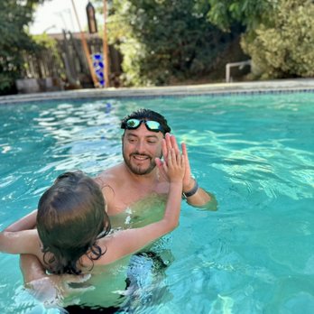 Privateers instructor giving a young swimmer a high-five in a sunlit backyard pool