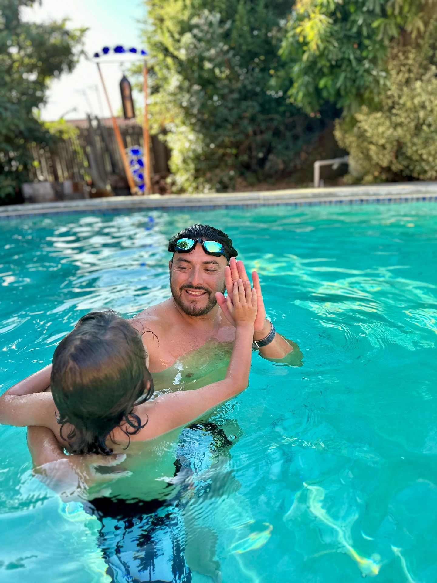 Privateers instructor giving a young swimmer a high-five in a sunlit backyard pool